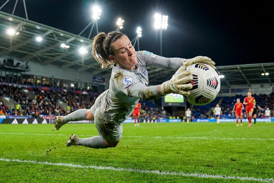 Goleira de futebol feminino realiza uma defesa em salto durante partida noturna