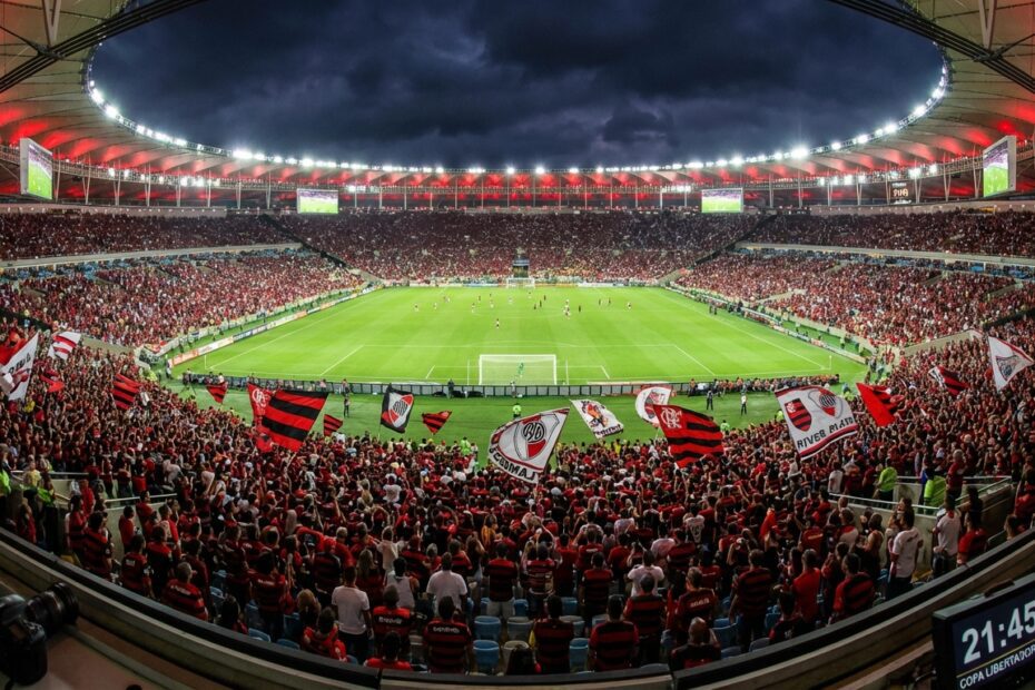 Estádio de futebol lotado e iluminado à noite com torcedores nas arquibancadas