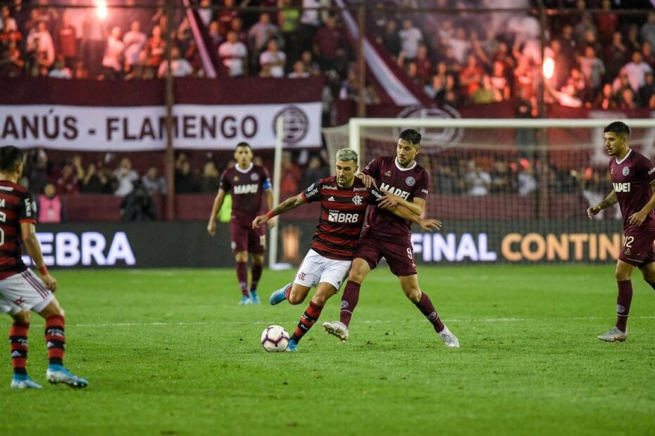 Jogadores de Flamengo e Lanús em disputa de bola durante partida noturna no estádio Néstor Díaz Pérez